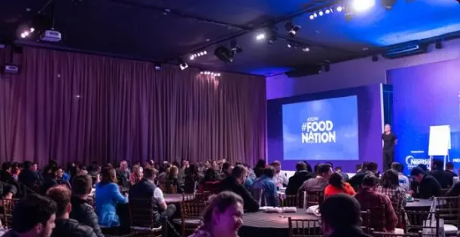 Auditório lotado do Acelera Food Nation com palco iluminado de roxo