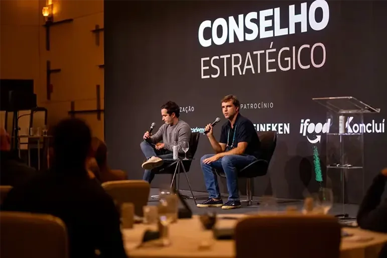 Conselho estratégico — dois empresários ao microfone no palco