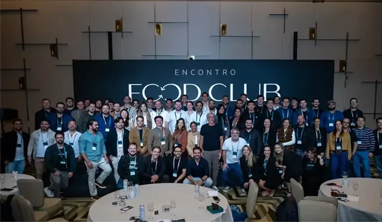 Foto de grupo do encontro Food Club em frente ao painel oficial