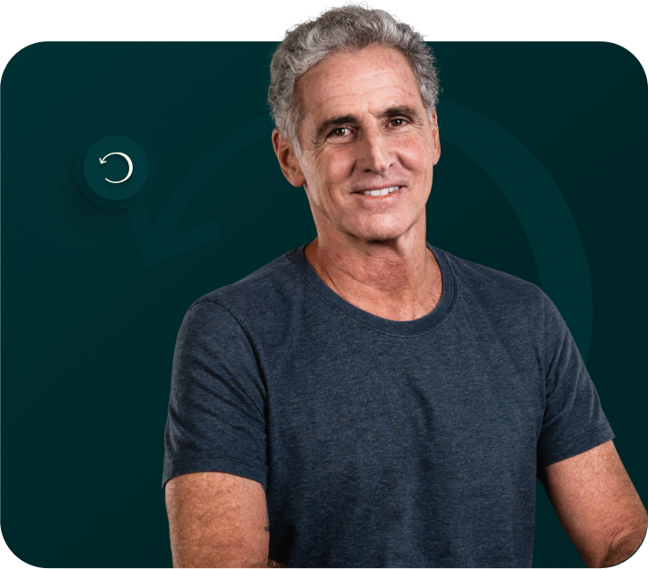 Um homem mais velho, de cabelos grisalhos, está em pé contra um fundo verde escuro, vestindo uma camisa azul escura de mangas curtas. Ele está sorrindo levemente e olhando diretamente para a câmera, como se estivesse dando as boas-vindas para você entrar no clube.